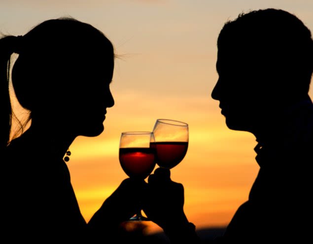 Silhouetted couple drink wine at sunset